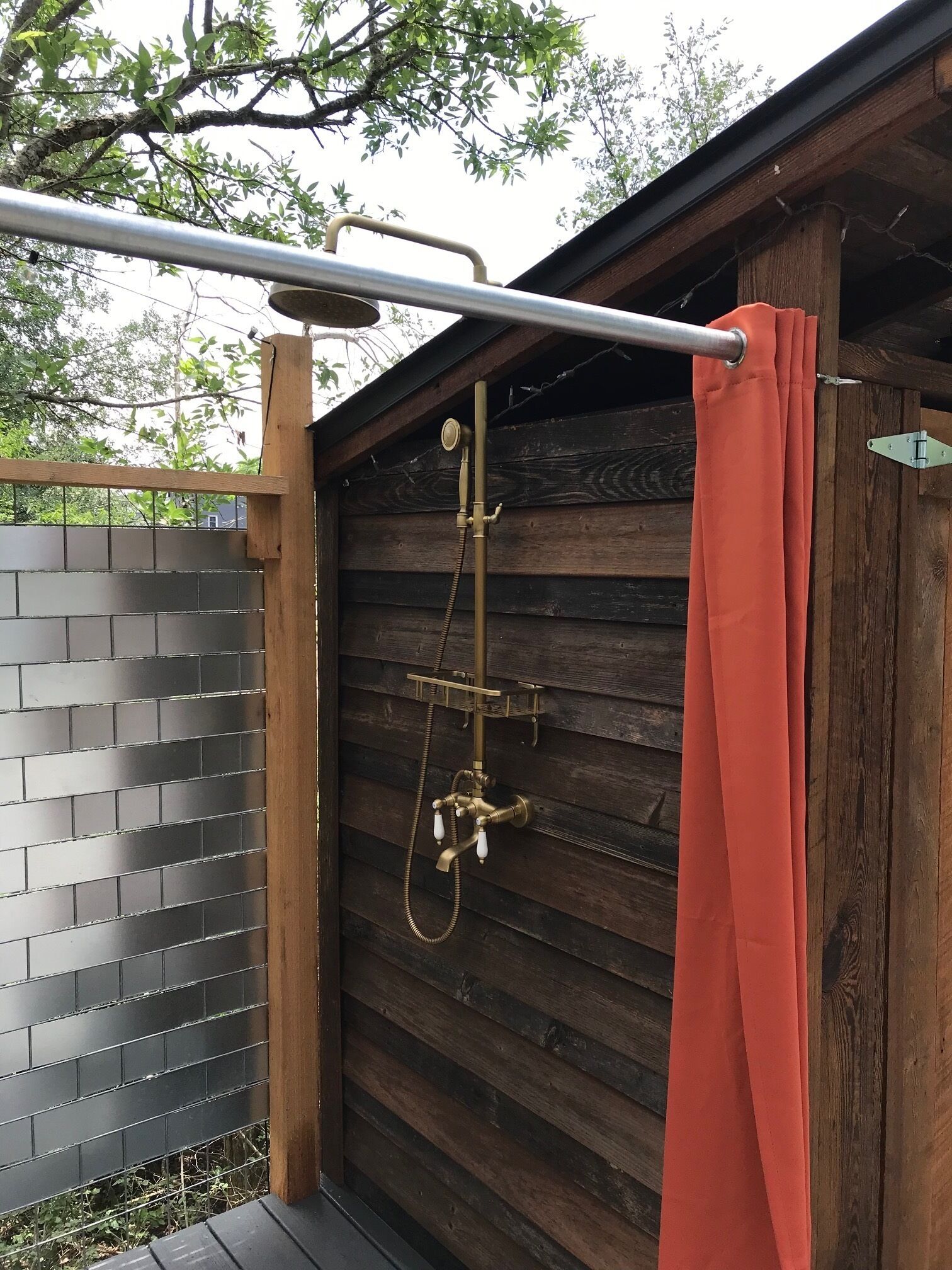A wooden cabin with a metal shower structure and a red curtain.