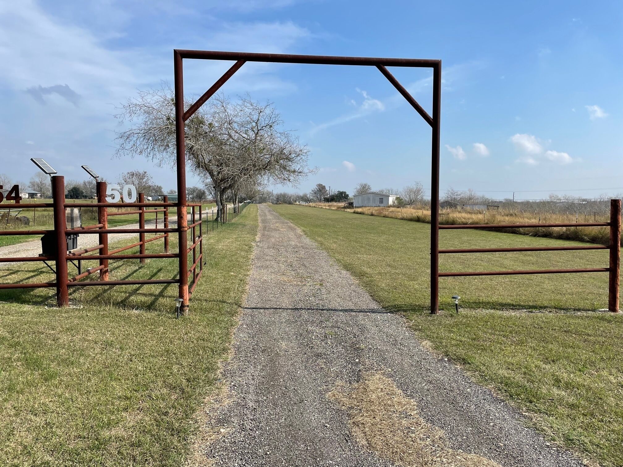 A gravel path leading through a fenced area with metal gates, trees, and a clear sky.