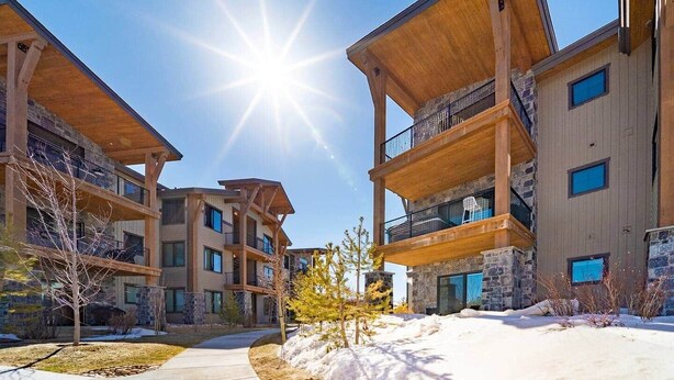 A modern multi-story building with balconies and large windows, surrounded by snow and trees.