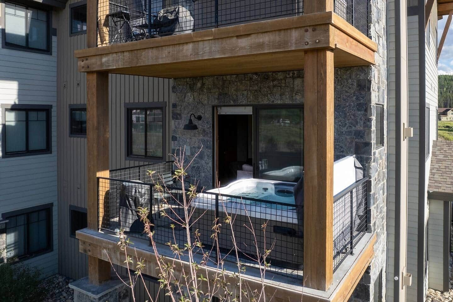 Een modern gebouw met een balkon, voorzien van een hottub, stenen muren en een houten terras.