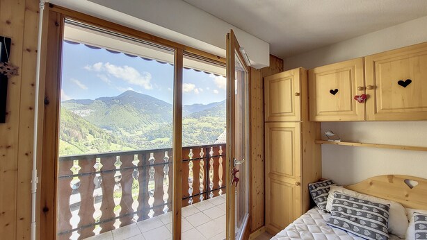 A room with a wooden balcony, a bed with patterned pillows, and wooden cabinets with heart-shaped cutouts. - Apartment 4 to 5 pers mountain view Grand Cerf 67 (Saint-Jean-d´Aulps)
