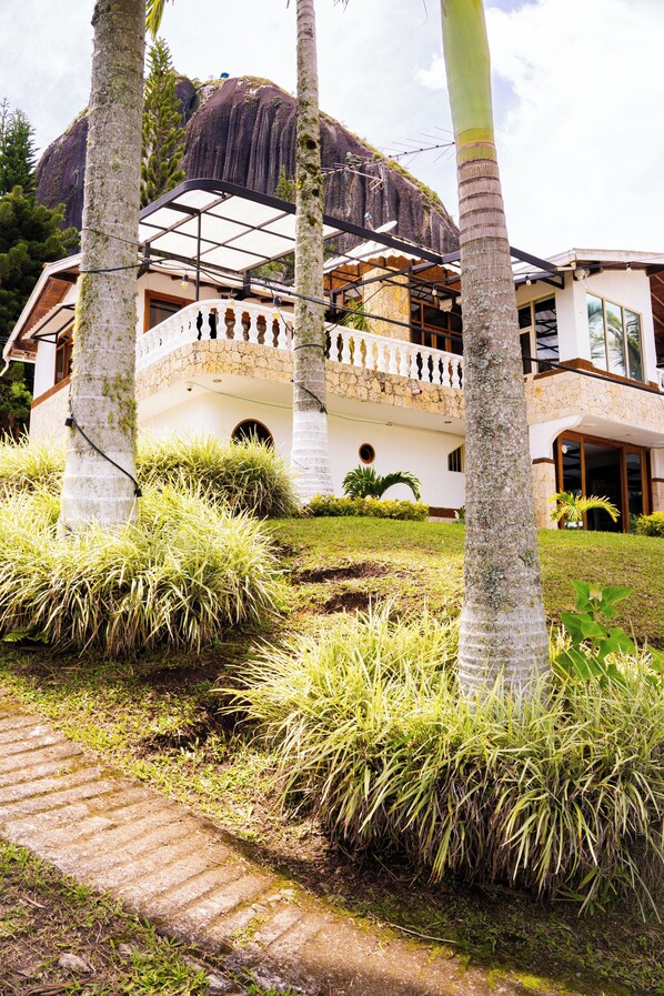 A large house with a stone facade, a balcony, and a thatched roof structure. - Casa Linda Guatapé (Guatapé)