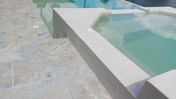 Een zwembad met betegeld zonneterras en een jacuzzi.