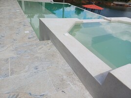A swimming pool with a tiled deck and a hot tub.
