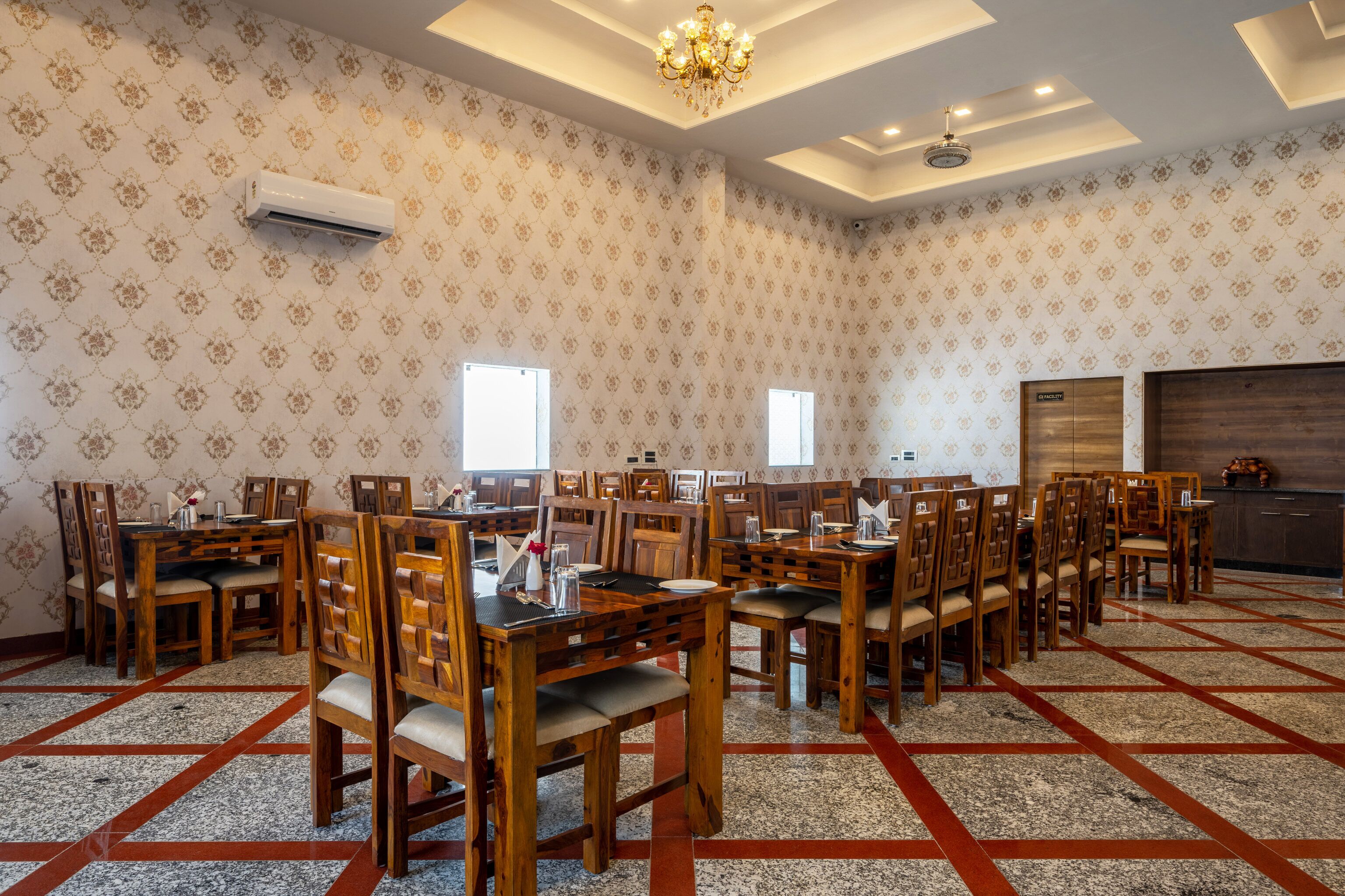 Un amplio comedor con varias mesas y sillas de madera, papel tapiz estampado y una araña.