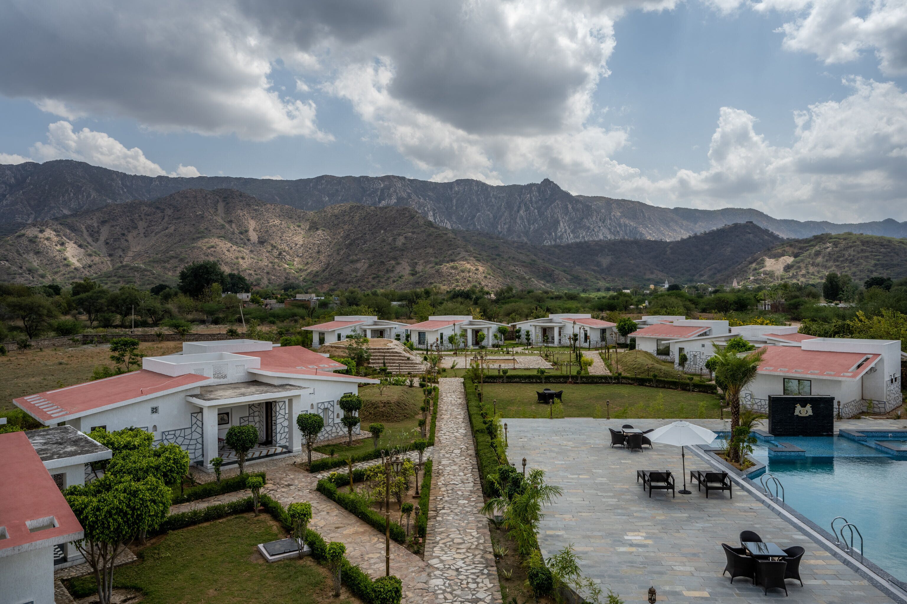 A resort with multiple white buildings, a swimming pool, and a mountainous backdrop.