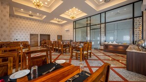 Uma sala de jantar ampla com várias mesas e cadeiras de madeira, um buffet e uma grande janela com treliça decorativa.