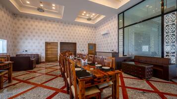 A spacious dining area with a long wooden table, multiple chairs, and a large window with decorative glass panels.