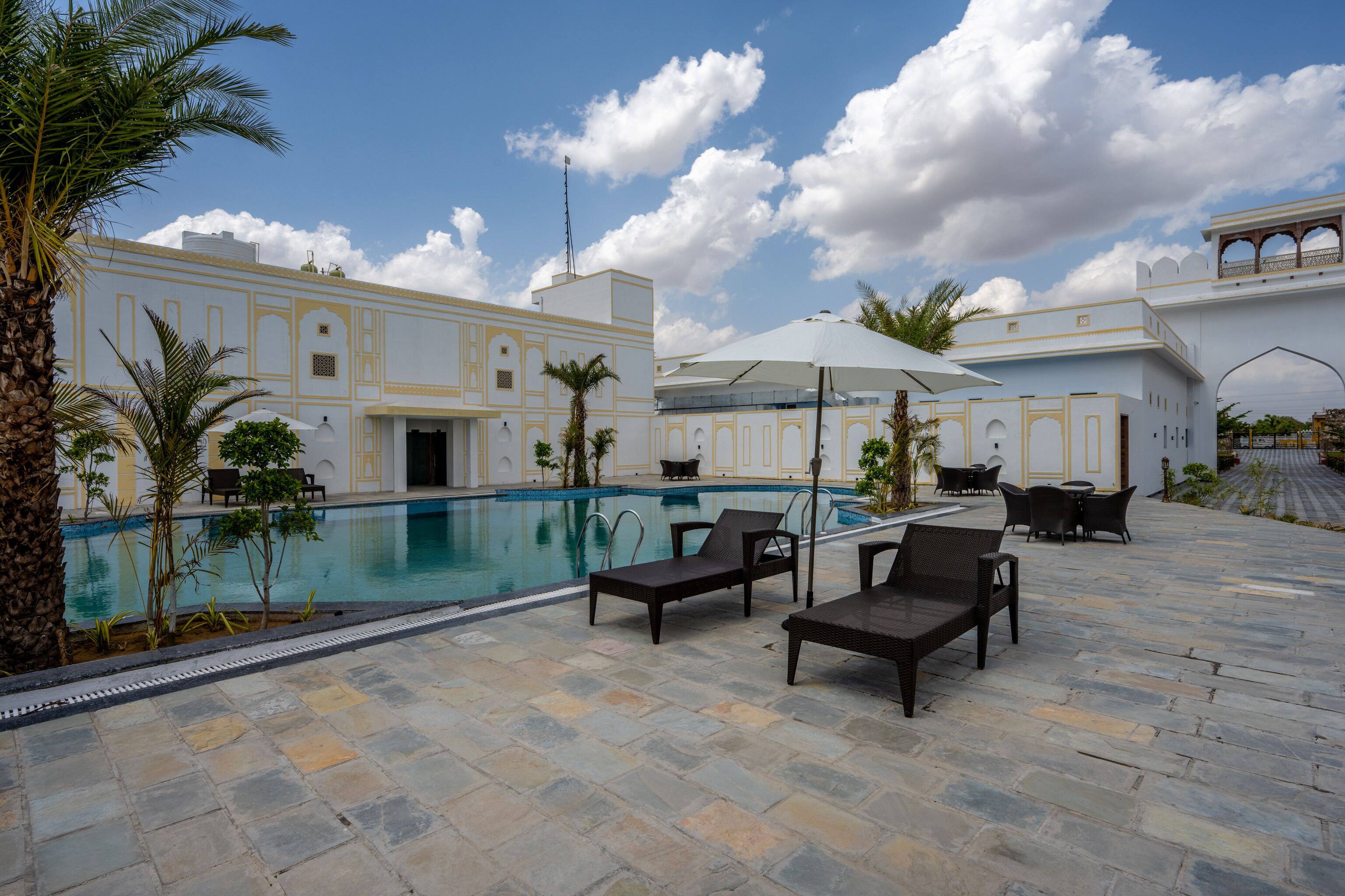 A poolside area with lounge chairs and umbrellas, a swimming pool, and a building with traditional architecture.