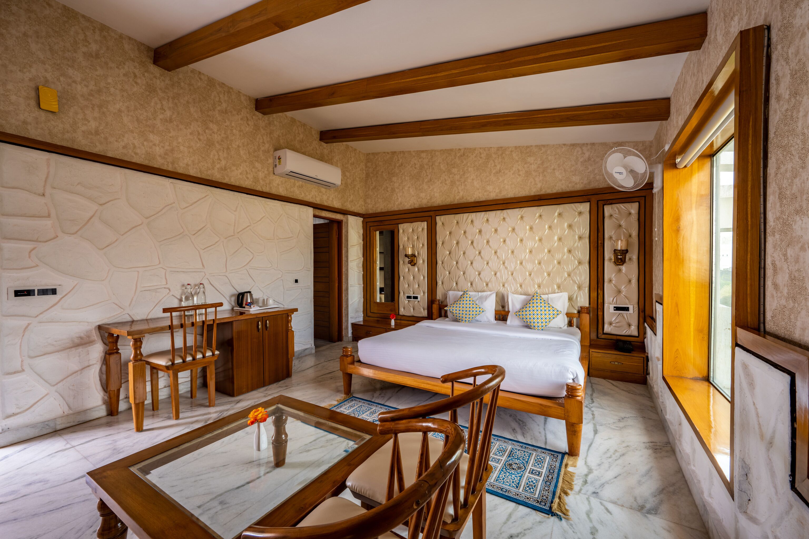 A hotel room with a bed, wooden furniture, a marble floor, and a stone wall.