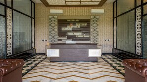 Uma área de recepção com balcão de check-in, papel de parede estampado e piso com padrão em ziguezague.