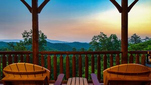 A wooden deck with two Adirondack chairs and a small table, overlooking a forested landscape. - Mega Views! 6 Miles to GSMNP! Hot Tub, Pool Table, Arcade, Foosball, 2Kg, 2QN (Sevierville)
