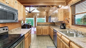 A wooden cabin kitchen with granite countertops, a stove, microwave, and a dishwasher. - Mega Views! 6 Miles to GSMNP! Hot Tub, Pool Table, Arcade, Foosball, 2Kg, 2QN (Sevierville)