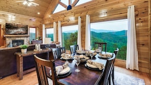 A wooden cabin interior with a dining area, large windows, and a fireplace. - Mega Views! 6 Miles to GSMNP! Hot Tub, Pool Table, Arcade, Foosball, 2Kg, 2QN (Sevierville)