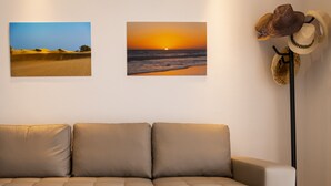 Un salon moderne avec un canapé d’angle beige, deux tableaux représentant des paysages encadrés accrochés au mur et une collection de chapeaux de cow-boy disposés sur un présentoir noir.
