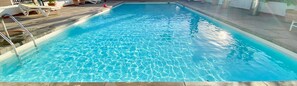 A rectangular swimming pool with clear water, surrounded by a tiled deck and potted plants.