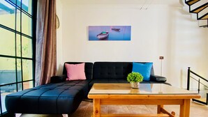 A modern living room with a black sectional sofa, a wooden coffee table, and a painting of boats on the wall.