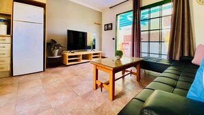 A living room with a sofa, a TV, a wooden table, and a refrigerator.