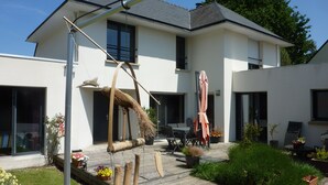 A modern two-story house with a patio area featuring a table and chairs, a hanging chair, and potted plants. - Maison Guidel, 5 mn de L'ocean (Guidel)