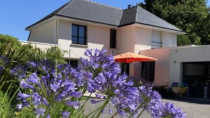 A modern house with a grey roof and white walls, surrounded by a garden with purple flowers. - Maison Guidel, 5 mn de L'ocean (Guidel)