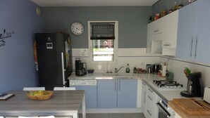 A compact kitchen with a refrigerator, dishwasher, stove, and a dining area with chairs and a table. - Maison Guidel, 5 mn de L'ocean (Guidel)