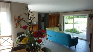 A living room with a blue sofa, a dining table with chairs, and a vase of flowers. - Maison Guidel, 5 mn de L'ocean (Guidel)