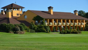 A large yellow building with multiple balconies and a central tower, surrounded by well-maintained lawns and greenery. - Golf Hotel Castelconturbia (Agrate Conturbia)