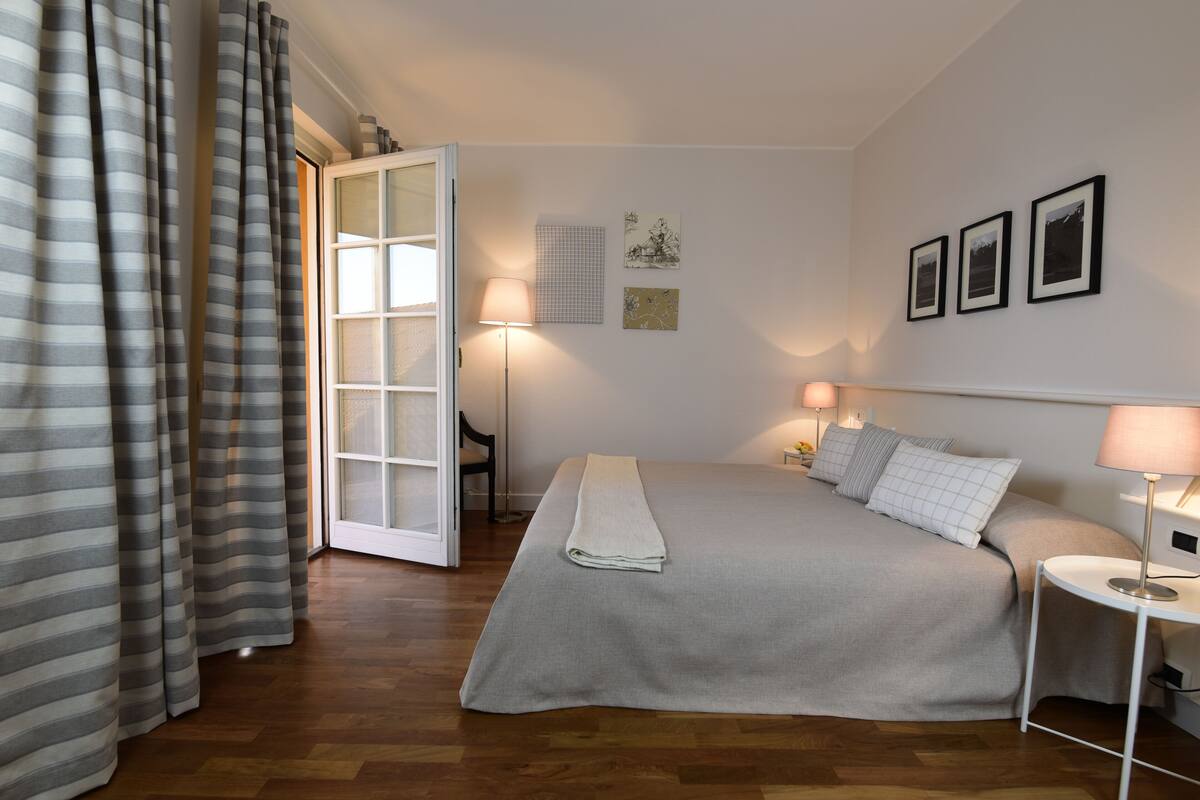Ein Schlafzimmer mit einem Bett, Nachttischlampen, einem Sessel und einer Tür zu einem anderen Raum.