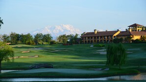 A golf course with a water hazard, a bridge, and a mountain in the background. - Golf Hotel Castelconturbia (Agrate Conturbia)