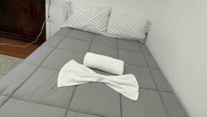 A bed with a grey quilt and two white pillows with a polka dot pattern.