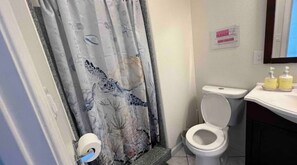 A bathroom with a toilet, a shower curtain with a nature pattern, a roll of toilet paper, and a sign on the wall. - Spacious 2BR Guesthouse for 8 - EV, Pool, 4 Beds (Tracy)