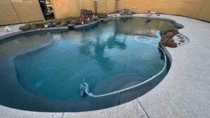 A swimming pool with a curved edge, surrounded by rocks and a small waterfall feature.