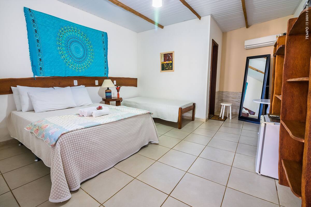 A bedroom with a large bed, a smaller bed, a wooden headboard, a nightstand, a mirror, a wardrobe, and a wall tapestry.