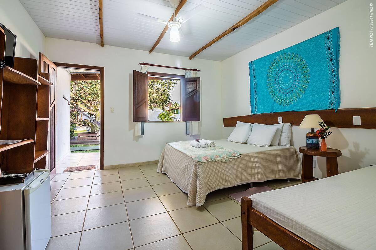 A bedroom with a bed, a nightstand, a window with curtains, a ceiling fan, and a view of the outside.