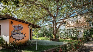 A courtyard with a mural, a tree, and a building with a tiled roof. - Pousada Galeão Santa Anna (Maraú)
