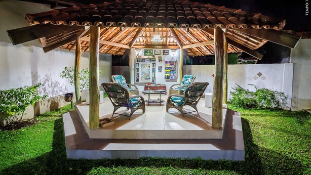 An outdoor patio with a tiled roof, two wicker chairs, a small table, and a refrigerator. - Pousada Galeão Santa Anna (Maraú)