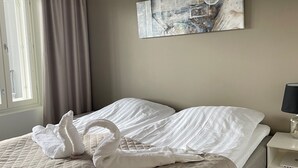 A neatly made bed with a quilted cover, a wall-mounted abstract painting, and a window with curtains. - Spa Hotel Red Aparments (Kuopio)
