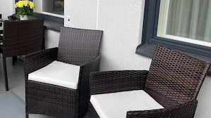 A patio area with wicker chairs and a table, a window with blinds, and a potted plant with yellow flowers. - Spa Hotel Red Aparments (Kuopio)