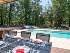 Un espace extérieur aménagé pour les repas, avec une piscine, le tout entouré d’arbres.