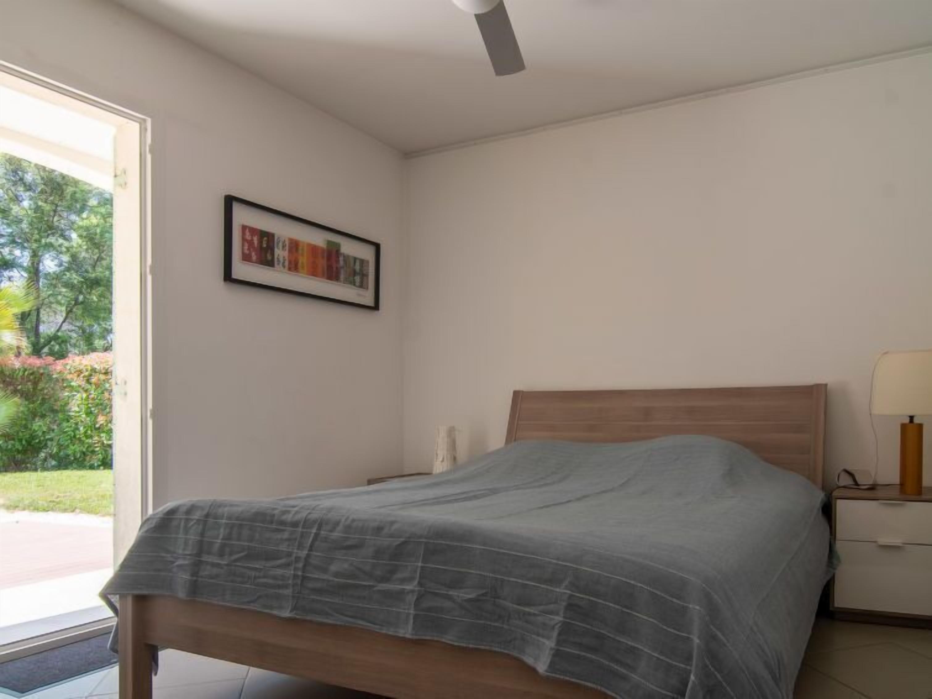 A bedroom with a bed, a nightstand, a lamp, and a door leading to a garden.