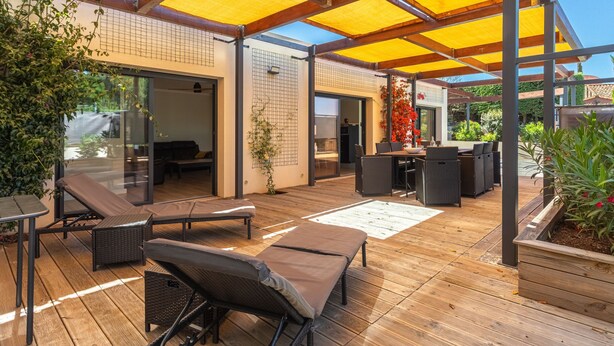 Un patio exterior con suelo de madera, sillones de descanso y una zona de estar cubierta.