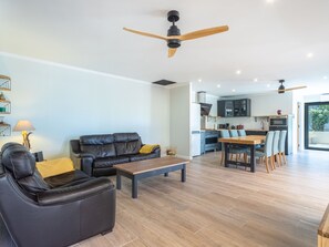A modern living room with a leather sofa, a wooden coffee table, and a dining area with a wooden table and chairs. There are ceiling fans and a kitchen in the background. - Maison Flocy by Interhome (Le Lavandou)