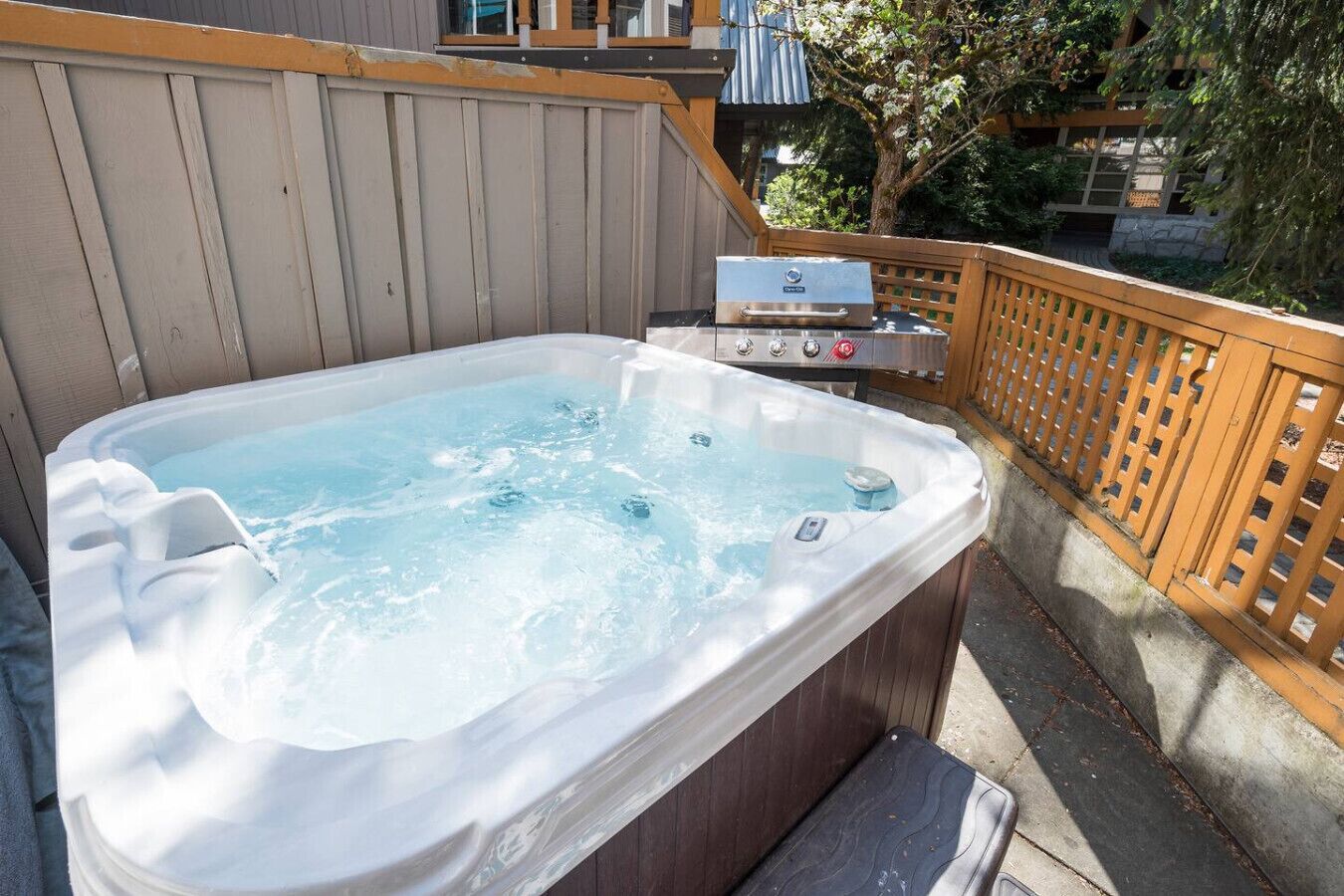 A hot tub with a built-in grill, surrounded by a wooden deck and a wooden fence.