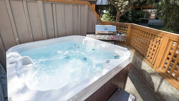 A hot tub with a built-in grill, surrounded by a wooden deck and a wooden fence.