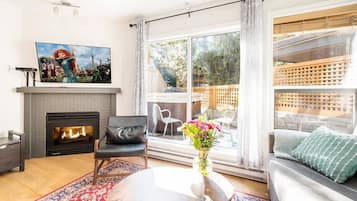 A modern living room with a fireplace, a large window with a view of the outdoors, a sofa, and a coffee table with a vase of flowers.