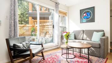 A living room with a sofa, a coffee table, a chair, a large window, and a decorative rug.