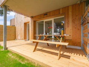 A wooden deck with a table and chairs, a glass door leading inside, and a wooden fence in the background.