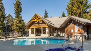 A pool area with two pools, a wooden building with a triangular gable, and a lifebuoy near the entrance. - Host Large Groups w/Best Location+Private Hot Tubs (Whistler)