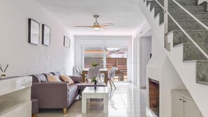 Un salon moderne avec un canapé, une table basse et un coin repas avec des chaises. Un escalier mène à un niveau supérieur.