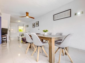 A modern dining area with a wooden table and chairs, a ceiling fan, and framed artwork on the walls.